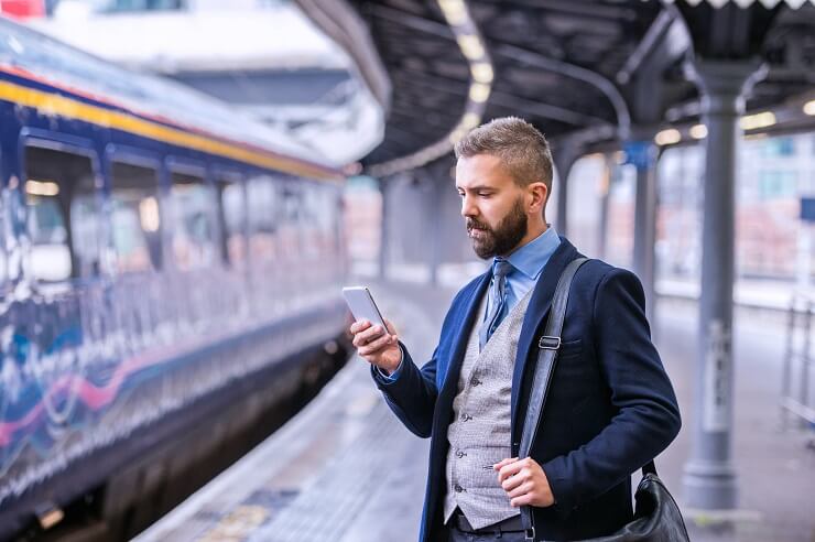 mężczyzna stojący na stacji kolejowej i przeglądający internet za pomocą smartfona