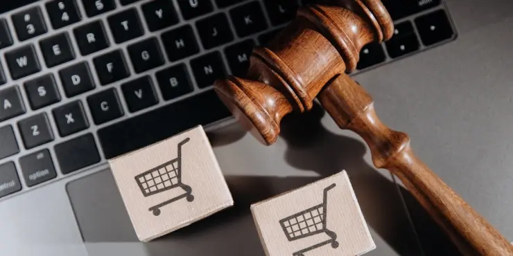 młotek sędziowski leżący na laptopie obok pudełek z zamówionymi produktami