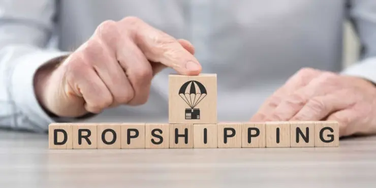 Osoba w białej koszuli układa kostki z napisem dropshipping